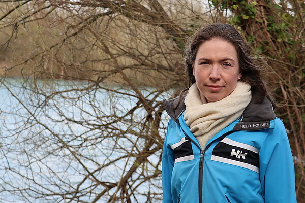 Anna in blue jacket standing in front of trees by a lake